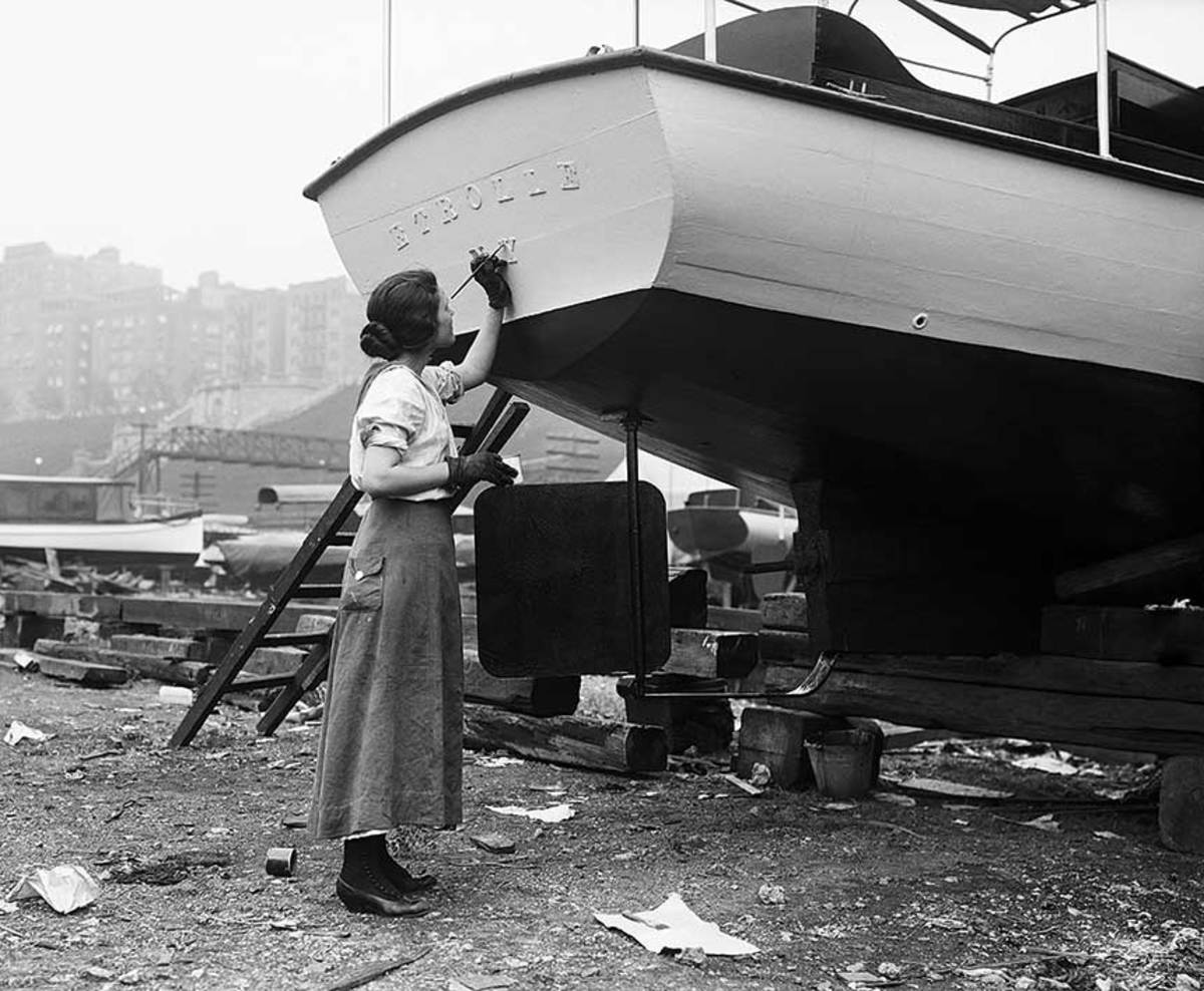A woman letters a boat’s name on the transom in this 1916 photo.