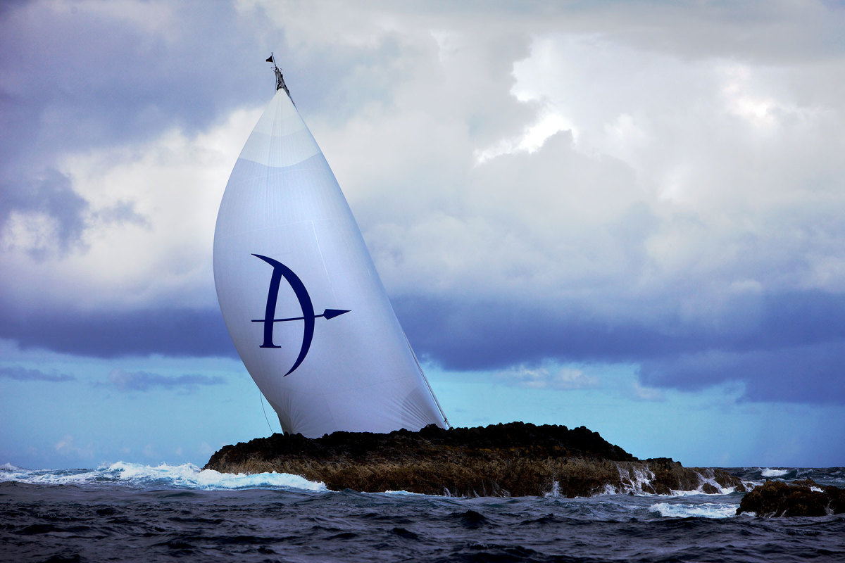 A superyacht at the St Barths Bucket Regatta races past a rocky outcropping.